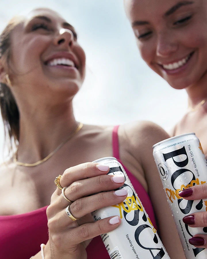 Two women holding POSCA Hydrate drink cans outdoors.