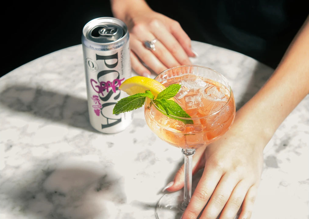 Posca Hydrate Grape in a cocktail glass with a lemon wedge and mint leaf, accompanied by a can of Posca Hydrate Grape on a marble surface.