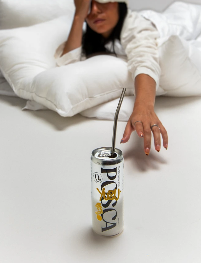 Person lying in bed reaching for a can of Posca Hydrate