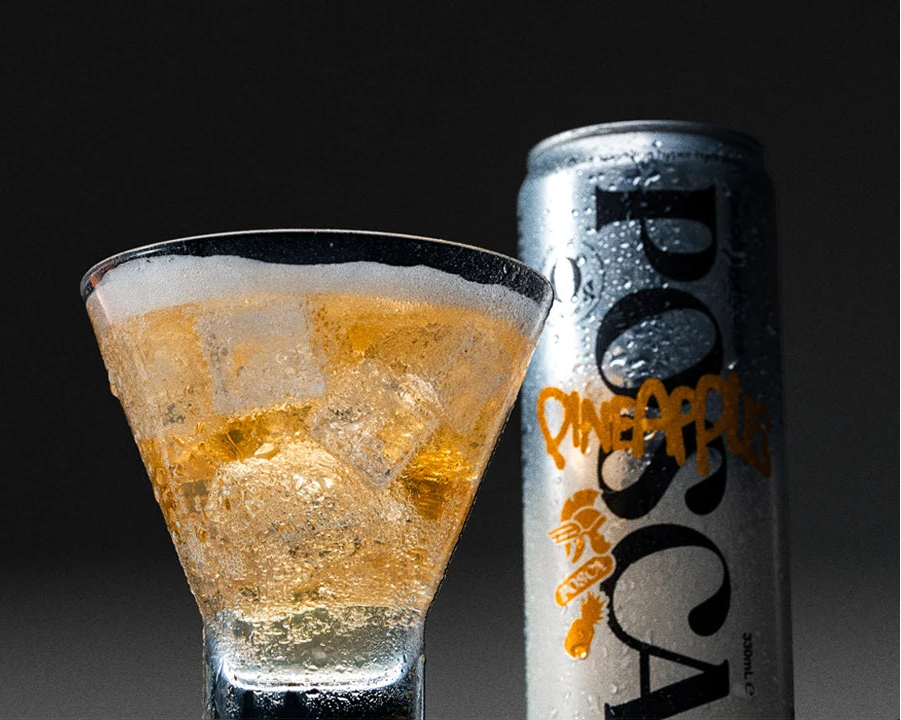 Glass of Posca Hydrate Pineapple with ice cubes next to a can on a dark background