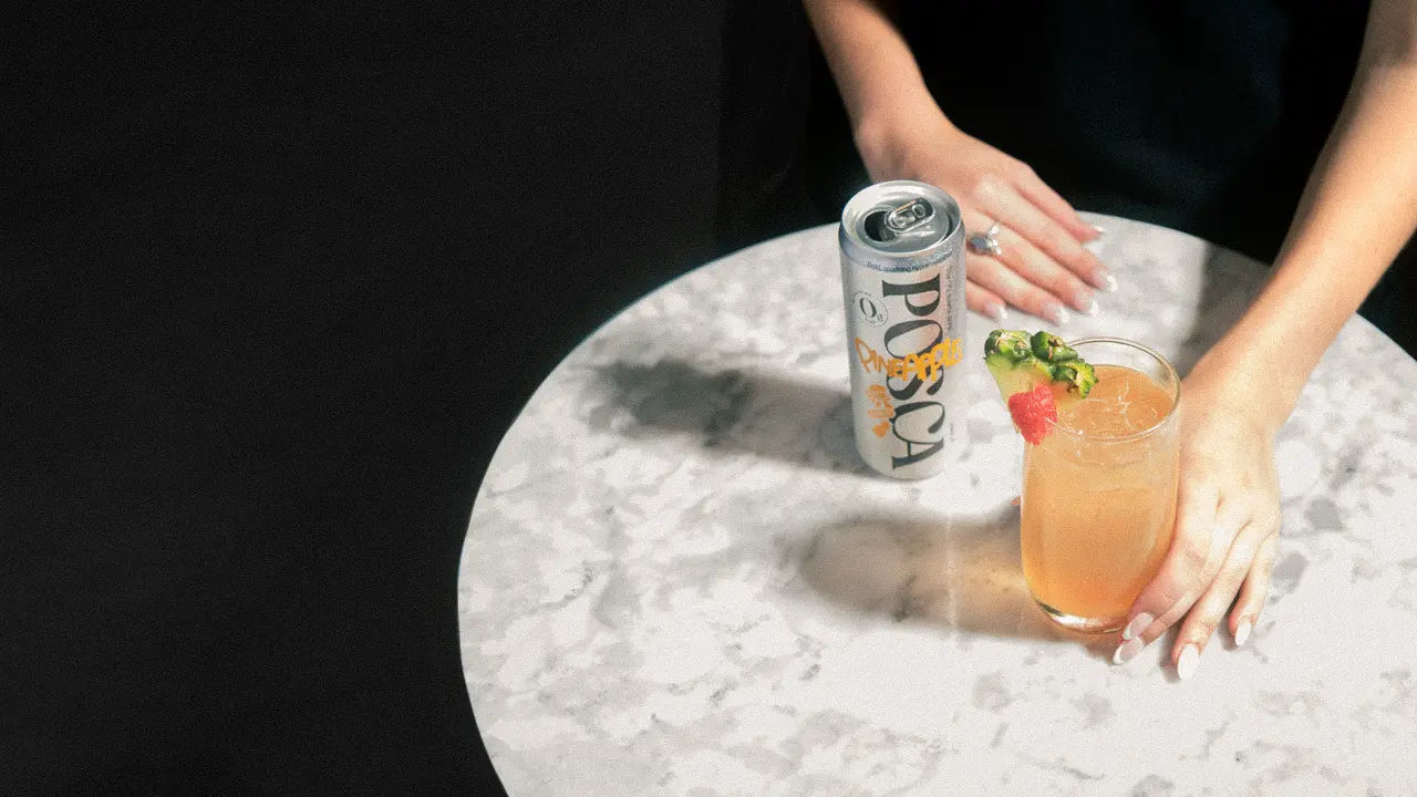 Person holding a cocktail with a can of Posca Hydrate on a marble table.
